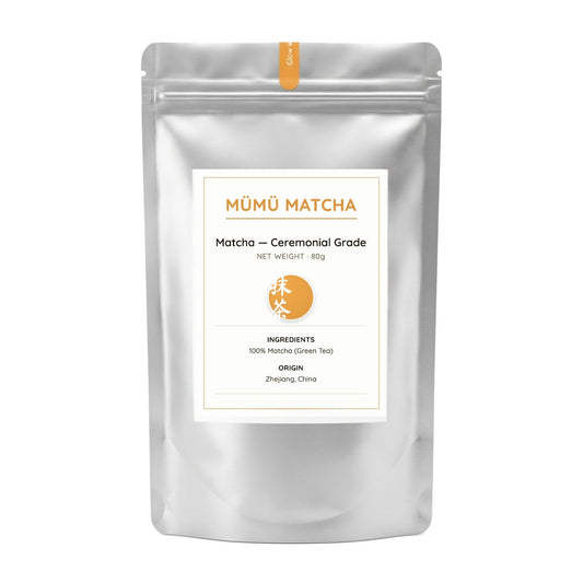 A silver stand-up pouch of MōMō Matcha ceremonial grade matcha tea, featuring a white label with orange text and a small orange circular logo, set against a plain white background.